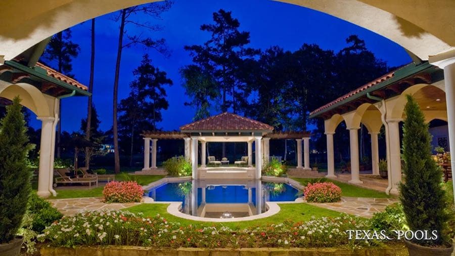 Custom luxury pool with lit gazebo and reflecting water at dusk, built by Texas Pools